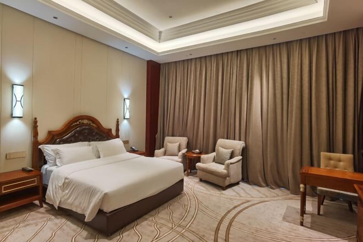 Ein Hotelzimmer mit einem großen Bett, zwei Sesseln, einem kleinen Tisch und einem Vorhang im Hintergrund.