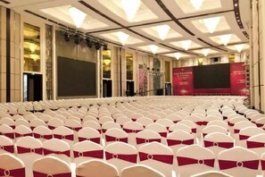 A large auditorium with rows of white chairs, a stage with a large screen, and a red banner.
