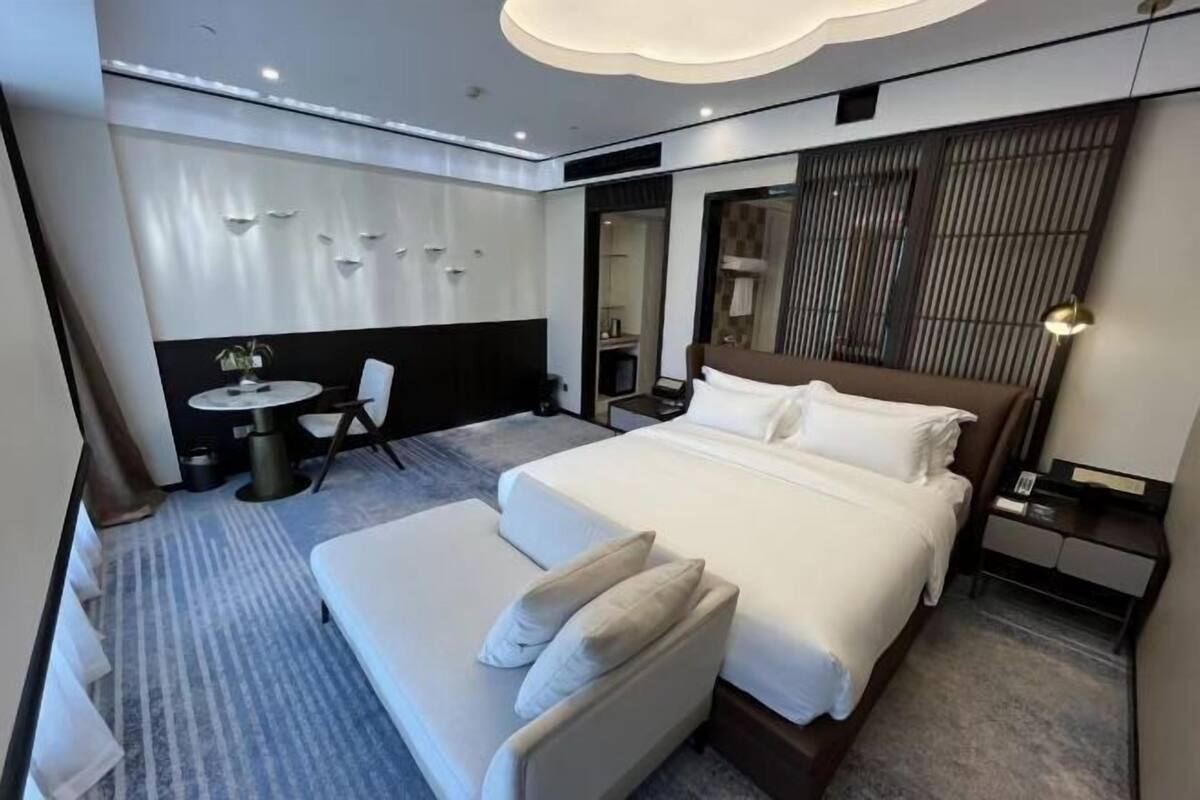 Ein modernes Hotelzimmer mit einem großen Bett, einer Couch, einem kleinen runden Tisch und einem Spiegel.
