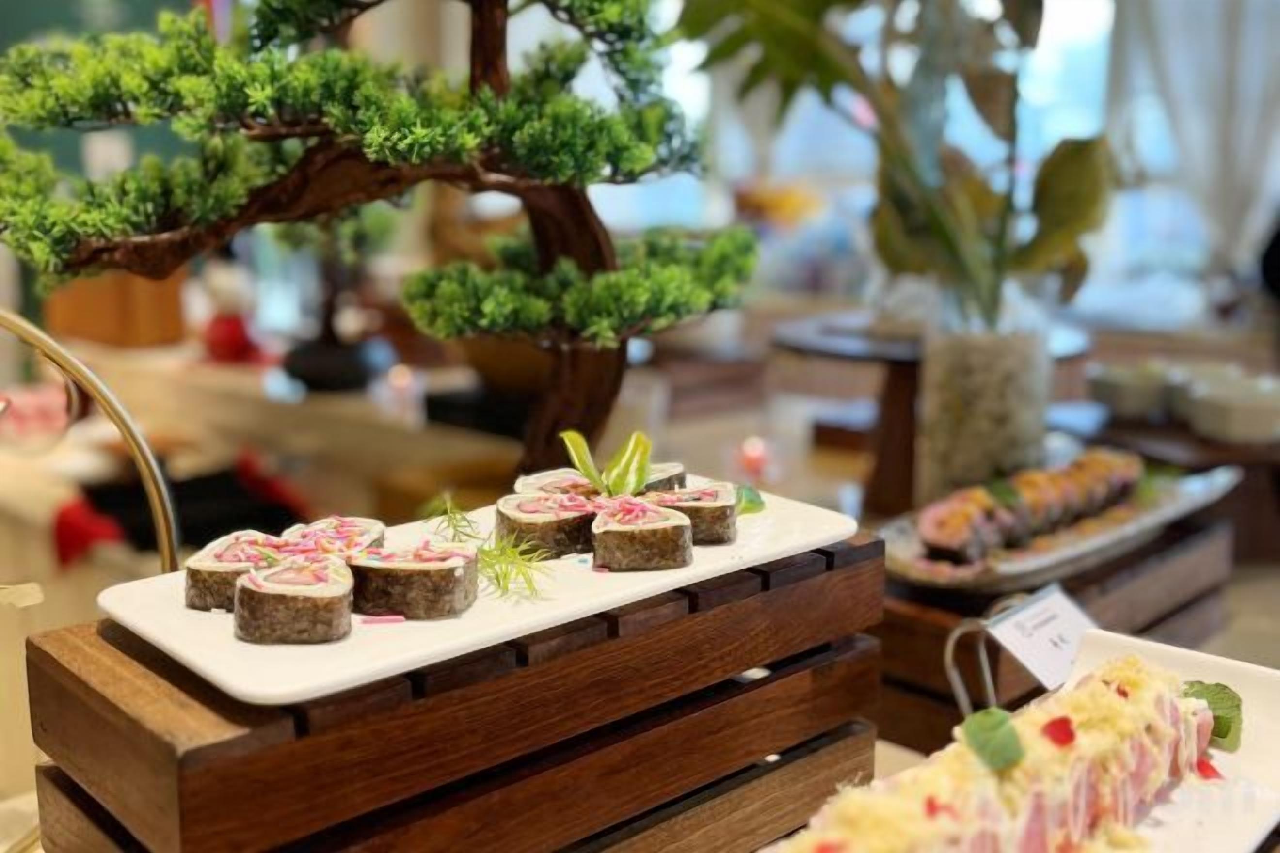 Élelmiszerekből összeállított kiállítás egy faállványon, a háttérben egy bonsai fával.