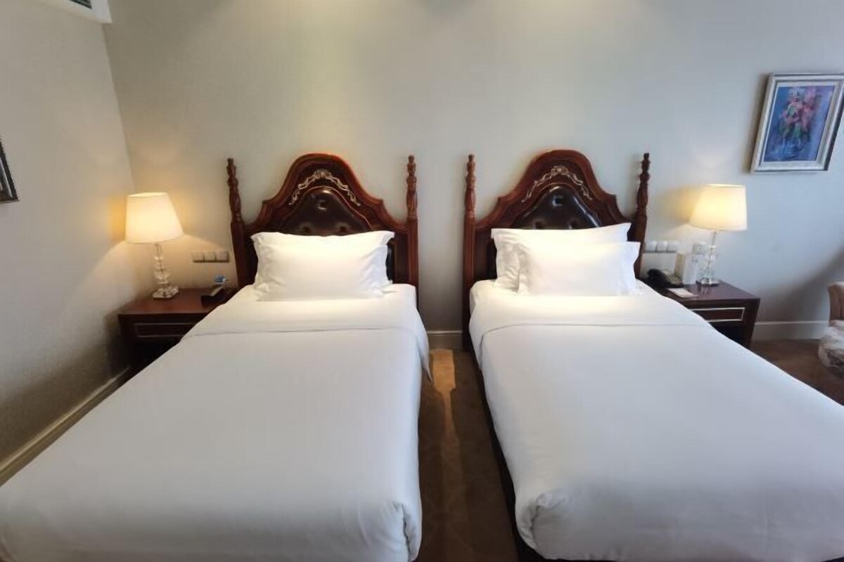 Ein Hotelzimmer mit zwei Einzelbetten, jeweils mit einem Holzkopfteil, weißer Bettwäsche und Nachttischlampen.