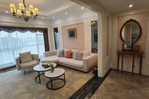 A modern living room with a sofa, armchair, and coffee table. There is a chandelier, a mirror, and a patterned rug.