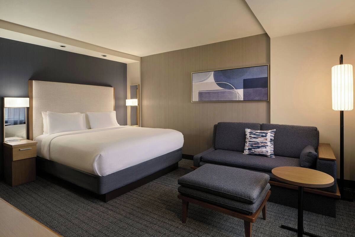 Une chambre d’hôtel moderne avec un grand lit, un canapé, une petite table et une lampe.