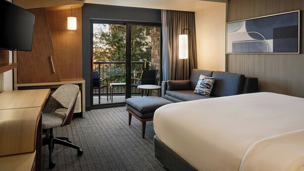 Une chambre d’hôtel comprenant un lit, un bureau, une chaise, un canapé, une télévision et un balcon avec des meubles d’extérieur.