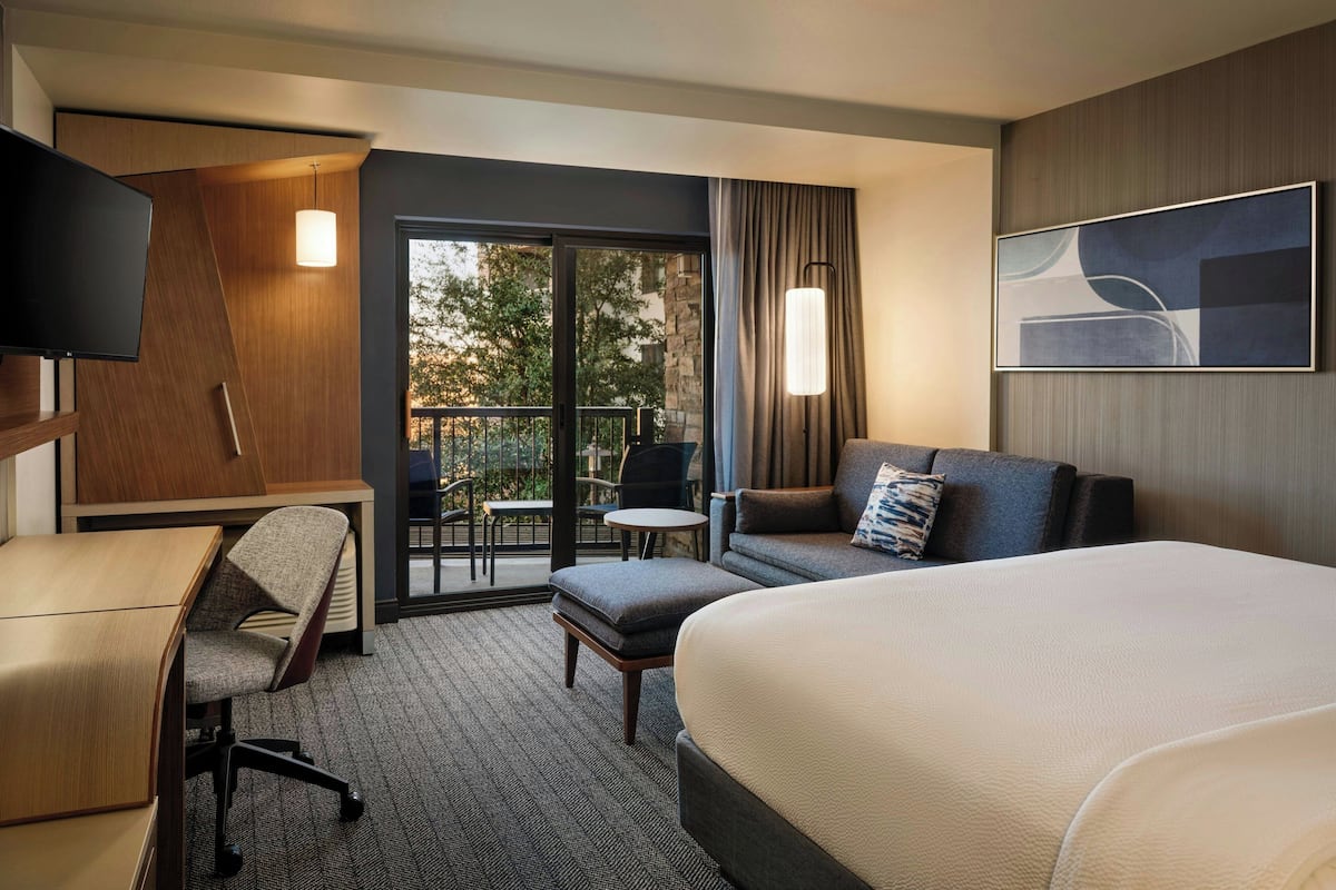 Une chambre d’hôtel comprenant un lit, un bureau, une chaise, un canapé, une télévision et un balcon avec des meubles d’extérieur.