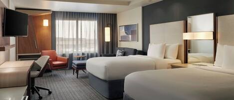 A hotel room with two beds, a desk, a chair, a TV, and a window with curtains.