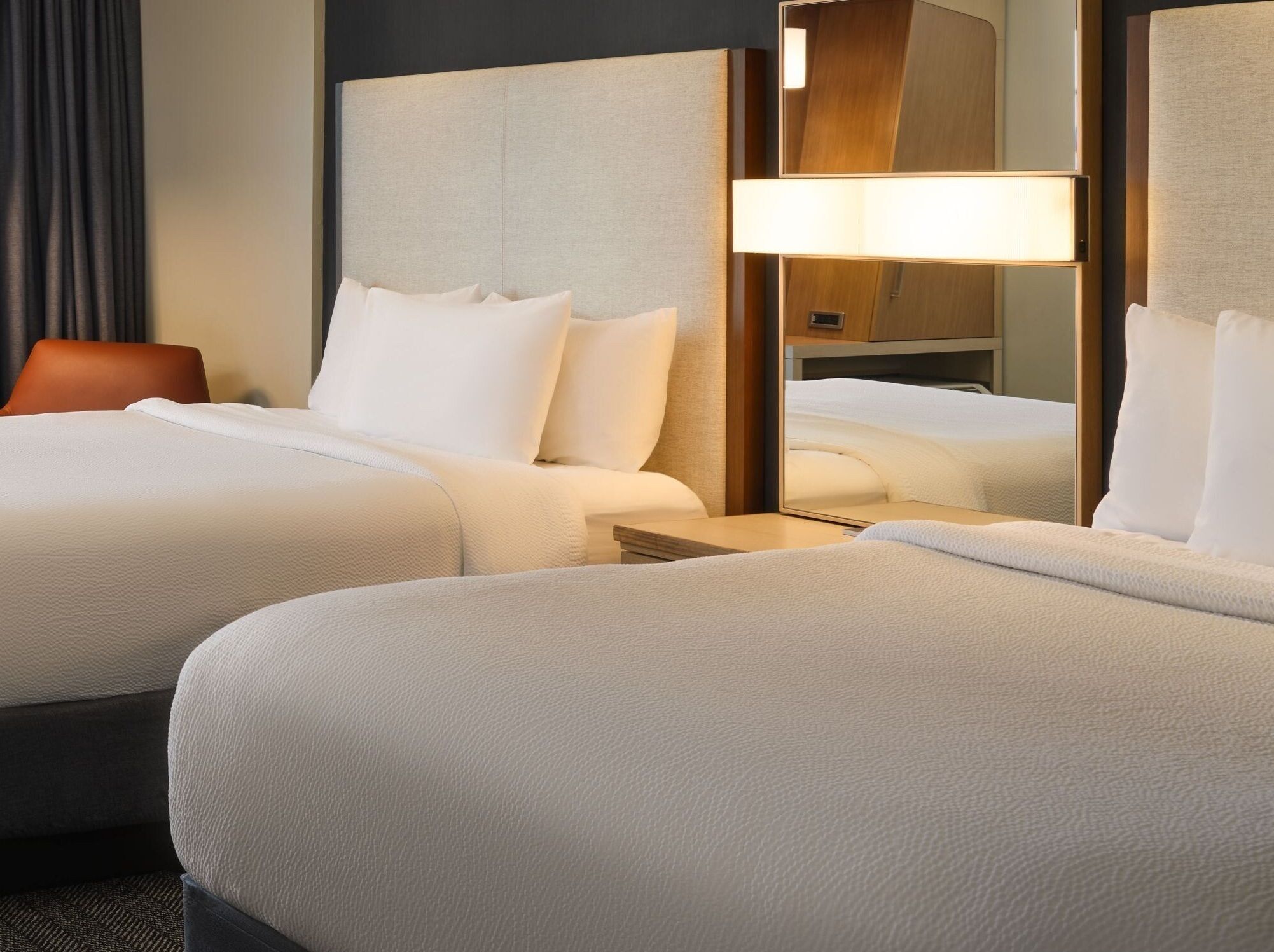 A hotel room with two beds, a nightstand, a lamp, and a mirror.