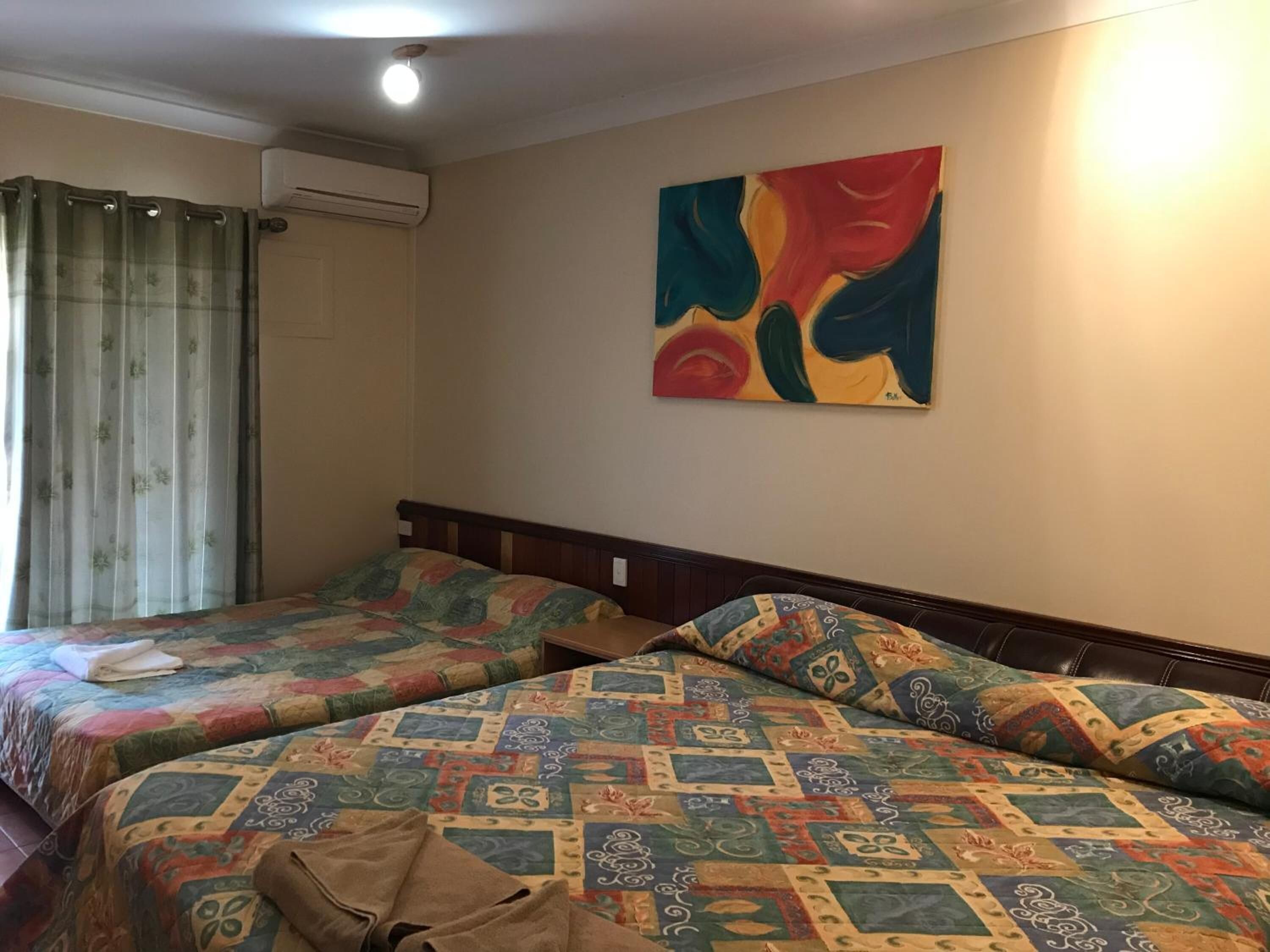 Une chambre d’hôtel avec deux lits, une peinture abstraite aux couleurs vives accrochée au mur et un appareil de climatisation.