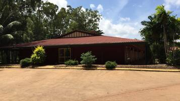 A red building with a metal roof, surrounded by trees and a large open parking area.