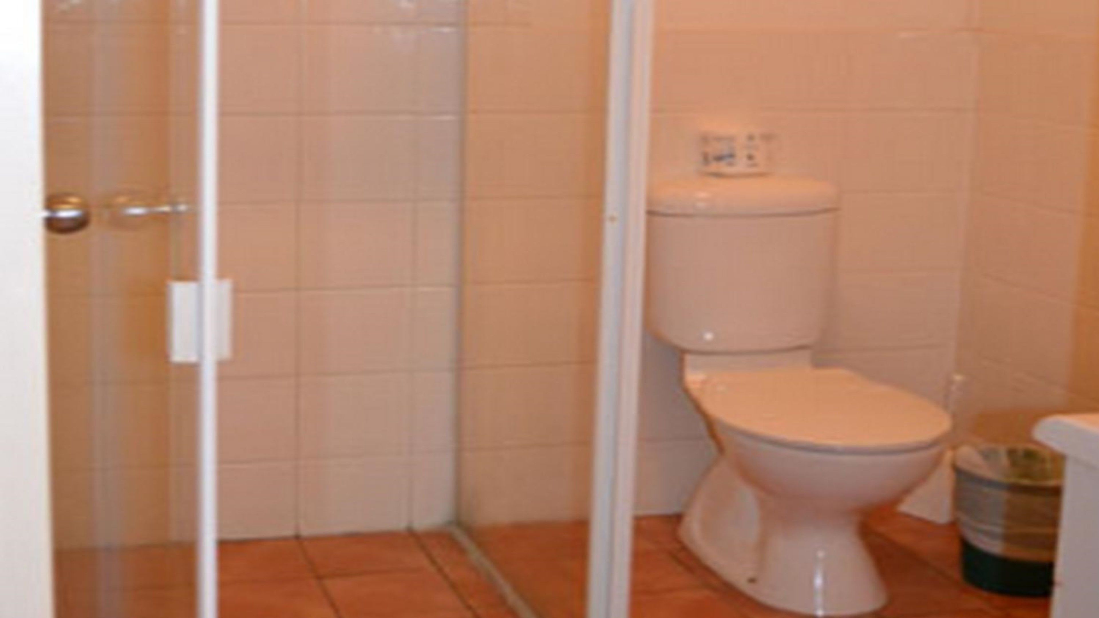 Un baño con inodoro, un cubo de basura y zona de ducha.