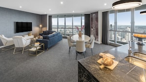 Una sala moderna con un televisor de pantalla plana, un sofá azul, una zona de comedor con una mesa redonda y una cocina con encimera de mármol.