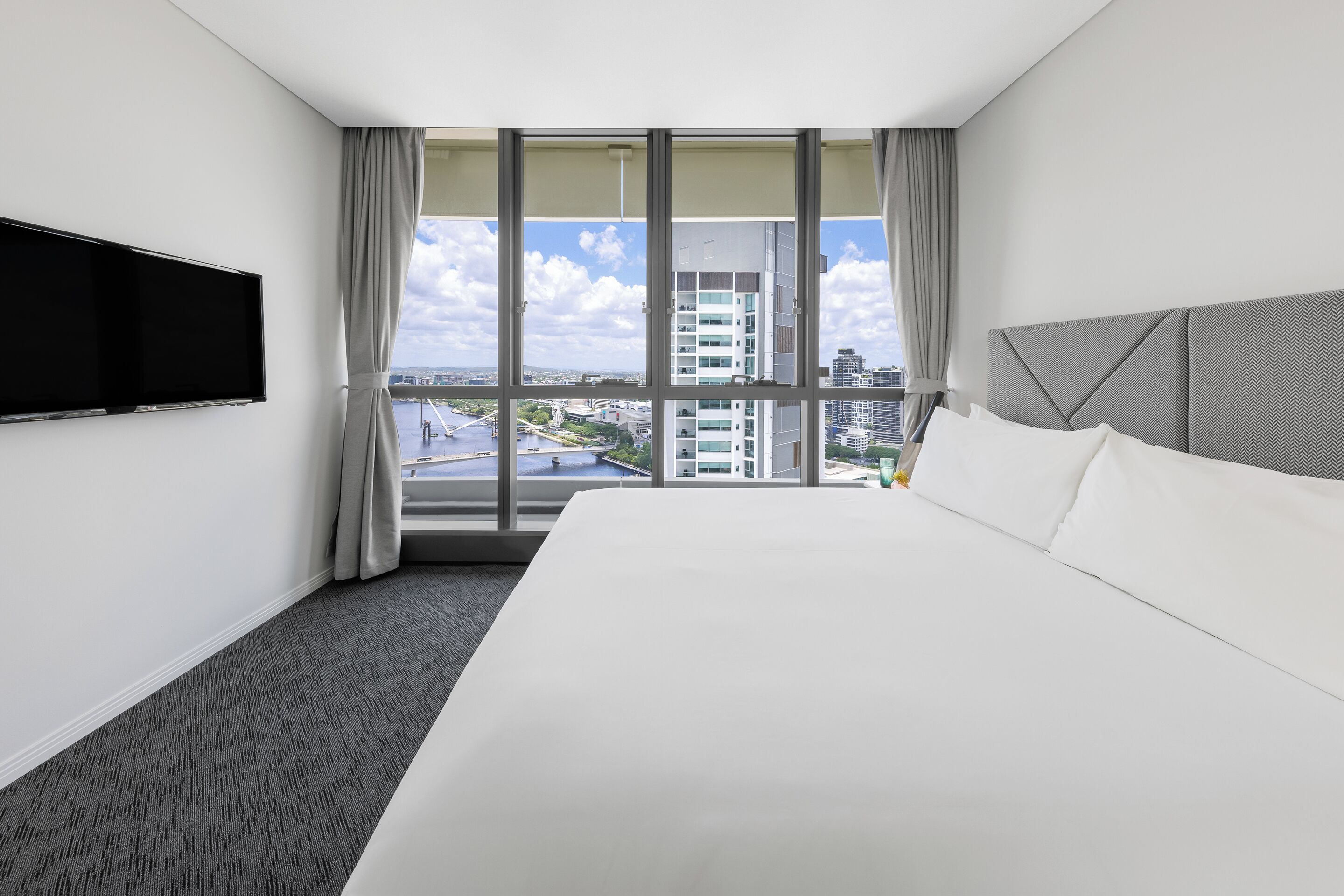 Une chambre d’hôtel dotée d’un grand lit, d’un téléviseur à écran plat fixé au mur et offrant une vue sur le paysage urbain grâce à de grandes fenêtres.