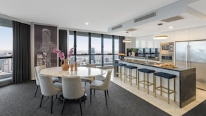 Una cocina moderna con una isla central, taburetes de bar y un amplio ventanal con vistas a un paisaje urbano.