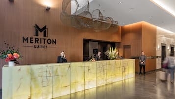Een hotel receptiebalie met een marmeren aanrecht, een grote decoratieve lamp en een bordje met 'Meriton Suites'.