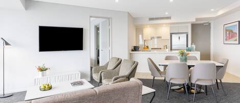 A modern living room with a flat-screen TV, a sofa, and a dining area with chairs and a table.