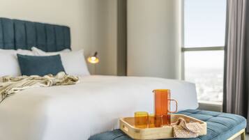 A neatly made bed with pillows, a bedside table with a tray holding glasses and a pitcher, and a view of the outdoors through a window.