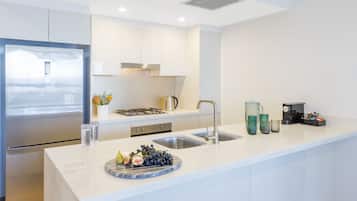 A modern kitchen with a stainless steel refrigerator, a gas stove, a sink, and a countertop with a fruit bowl and glasses.