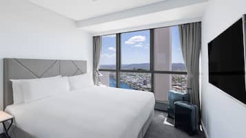 A hotel room with a large bed, a view of a cityscape, a TV, and a suitcase.