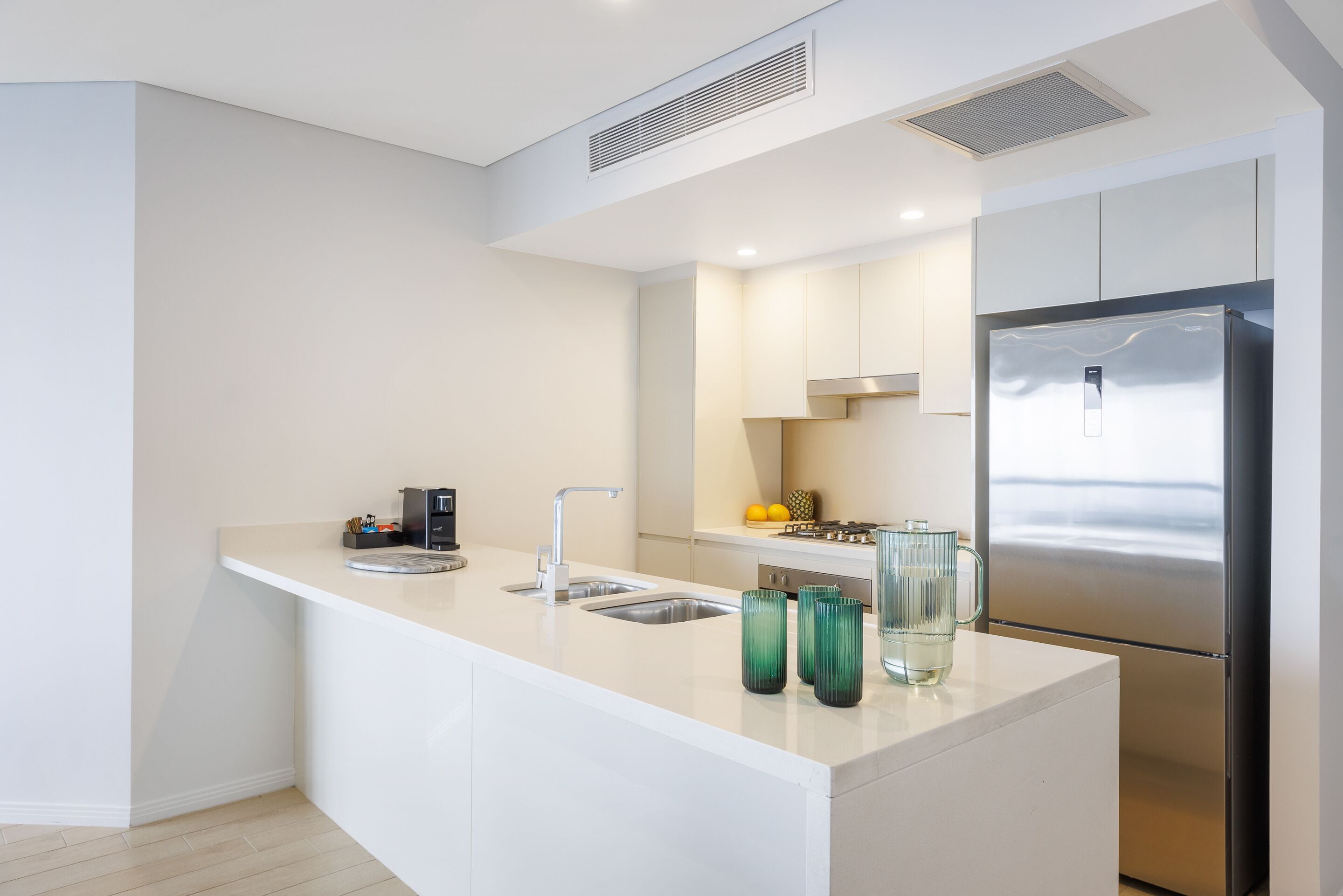 Una cocina moderna con encimera blanca, electrodomésticos de acero inoxidable y un lavabo integrado.