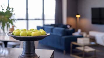 A modern living room with a dark-toned sofa, a coffee table with a bowl of green apples, and a large window providing natural light.