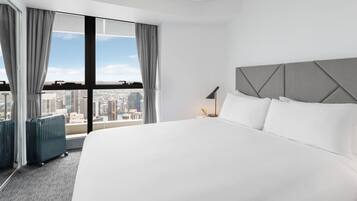 A hotel room with a large bed, a view of the city, and a suitcase.