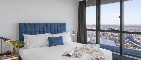 Habitación de hotel moderna con una cama grande, una mesita de noche, una lámpara y vistas a la ciudad a través de amplias ventanas.