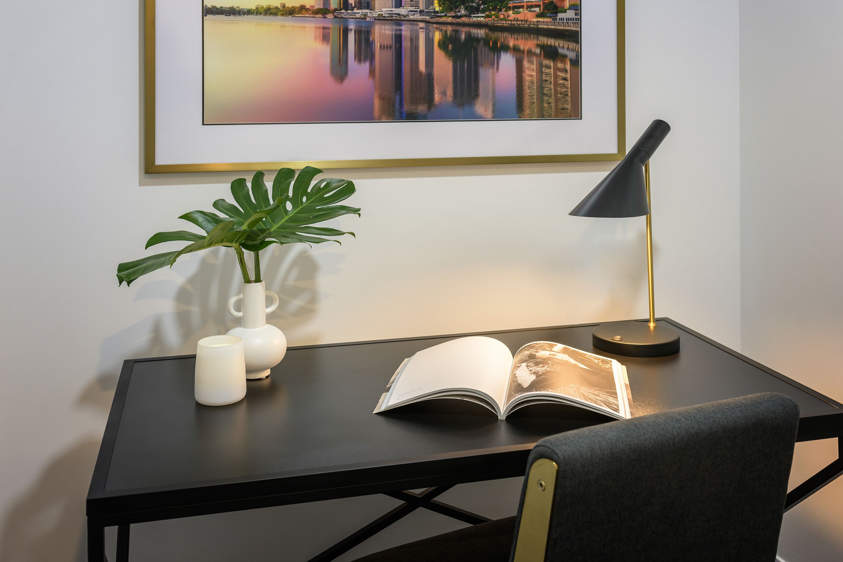 A desk with a book, a lamp, a plant, and a vase.