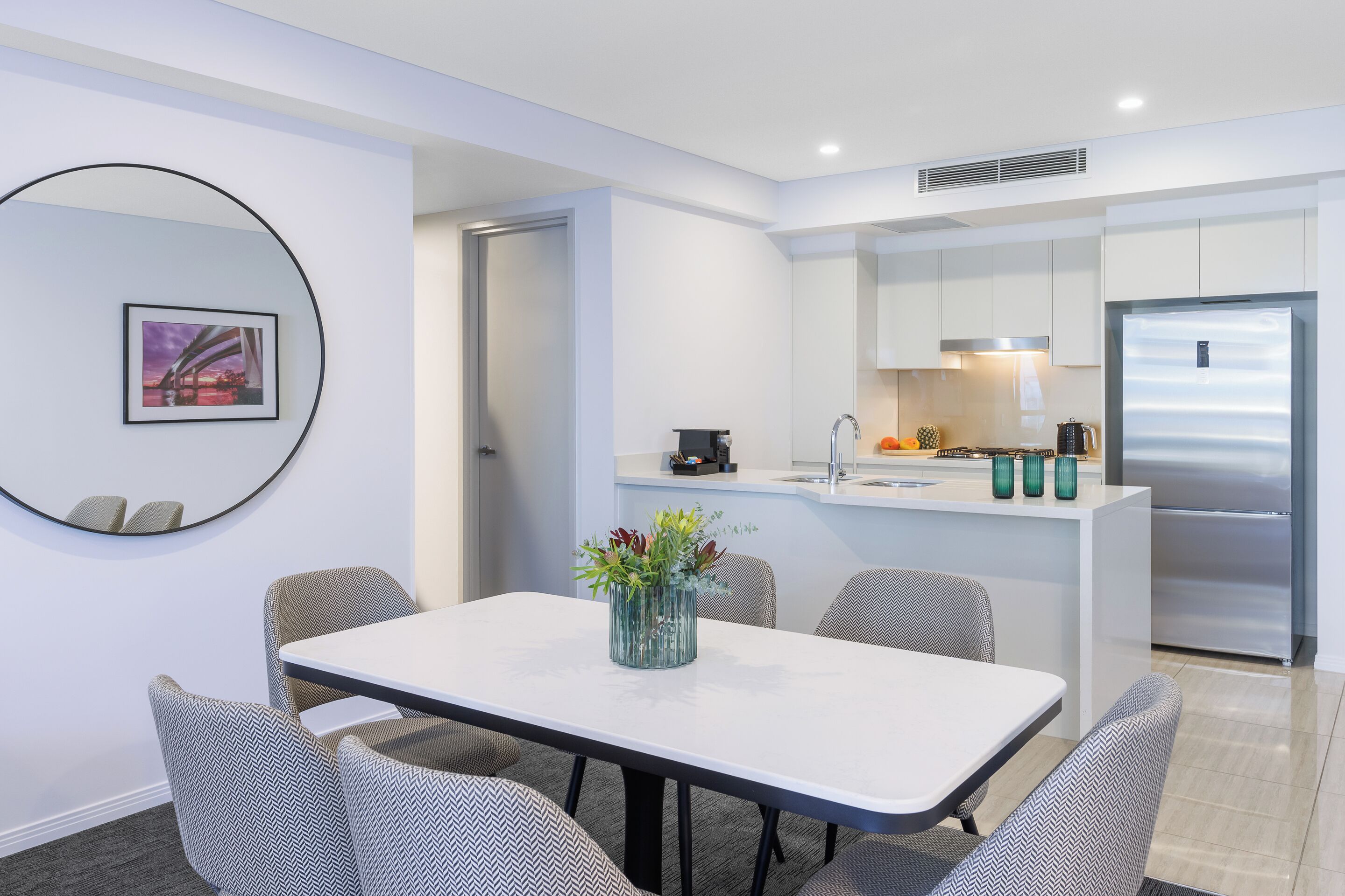 A modern kitchen with white cabinets, a stainless steel refrigerator, and a small island with a sink.