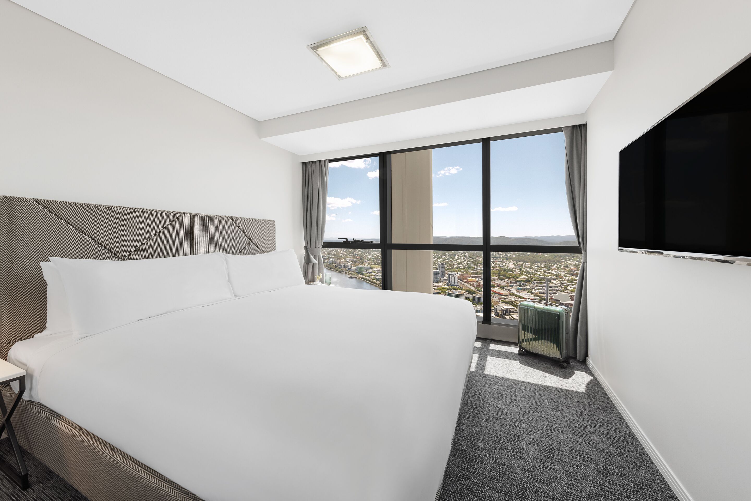Une chambre d’hôtel avec un grand lit, un téléviseur fixé au mur et une vue sur la ville grâce à de grandes fenêtres.
