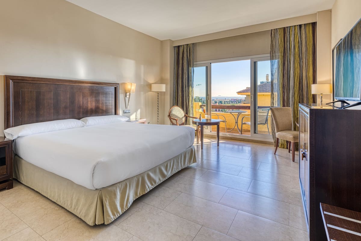 Een hotelkamer met een groot bed, een bureau met stoel, een televisie en een balkon met uitzicht.