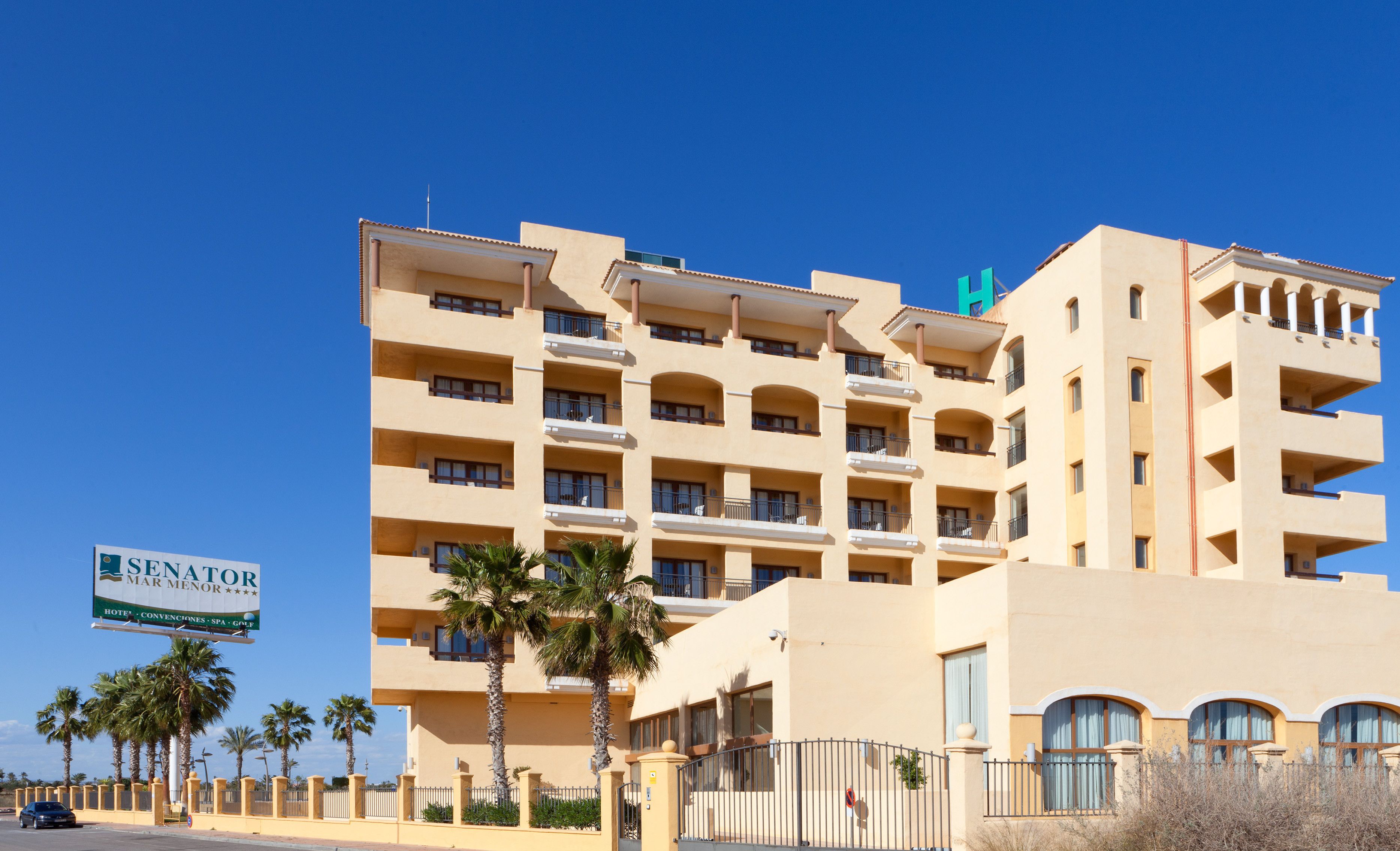 A multi-story hotel with balconies, palm trees, and a sign advertising amenities like a spa and golf.
