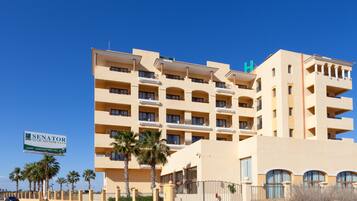 A multi-story hotel with balconies, palm trees, and a sign advertising amenities like a spa and golf.