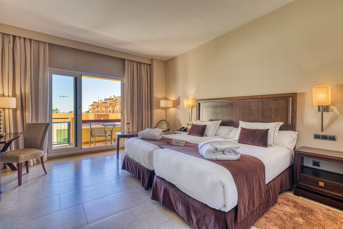 Een hotelkamer met een groot bed, een stoel, een bureau en een balkon met uitzicht op gebouwen.