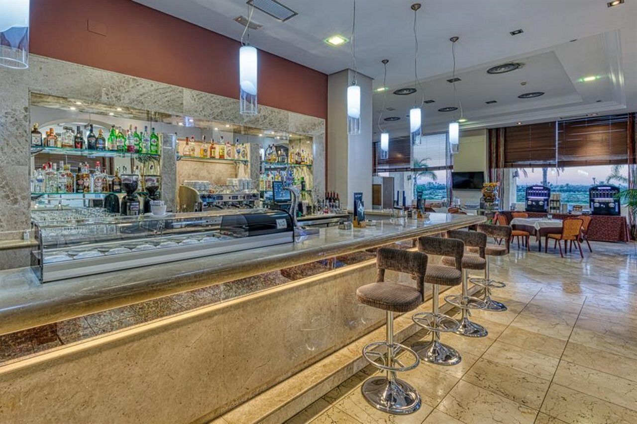 Zona de bar con mostrador de mármol, varias botellas de licor y taburetes.