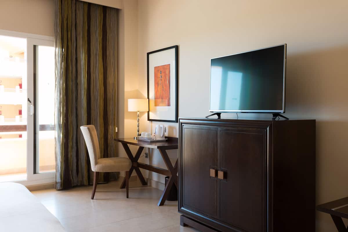Een hotelkamer met een bed, een bureau met stoel, een televisie op een kast en een groot raam met gordijnen.