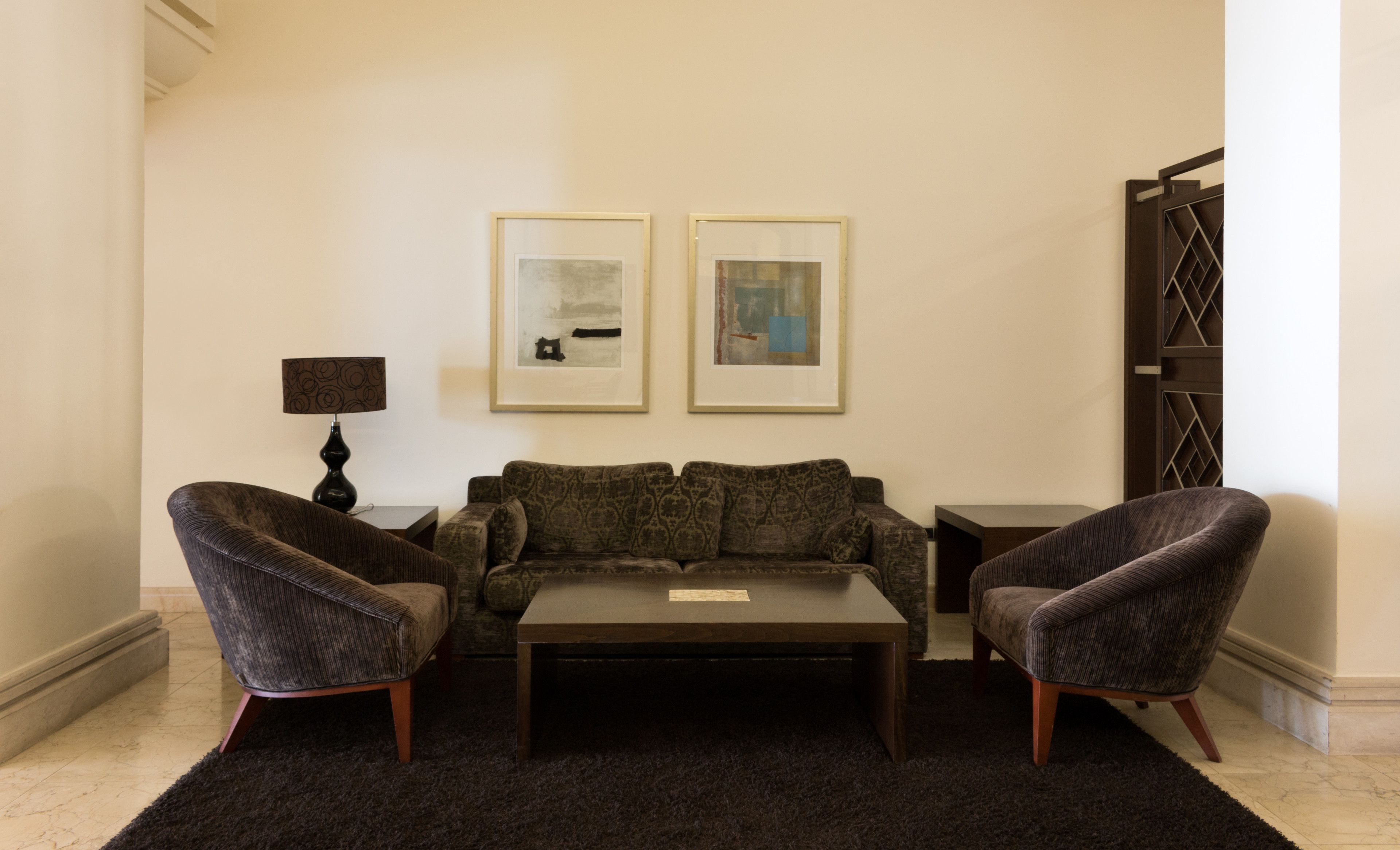 A living room with a dark-colored sofa, two armchairs, a coffee table, and two framed artworks on the wall.