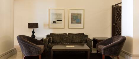 A living room with a dark-colored sofa, two armchairs, a coffee table, and two framed artworks on the wall.