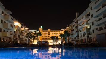 Un hotel con piscina, varios balcones y palmeras.