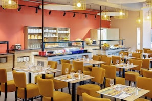 A restaurant with yellow chairs and tables, a buffet area with food and drinks, and a counter with a cash register. - Sowell Residences Les Chenes Verts (Saint-Raphael)