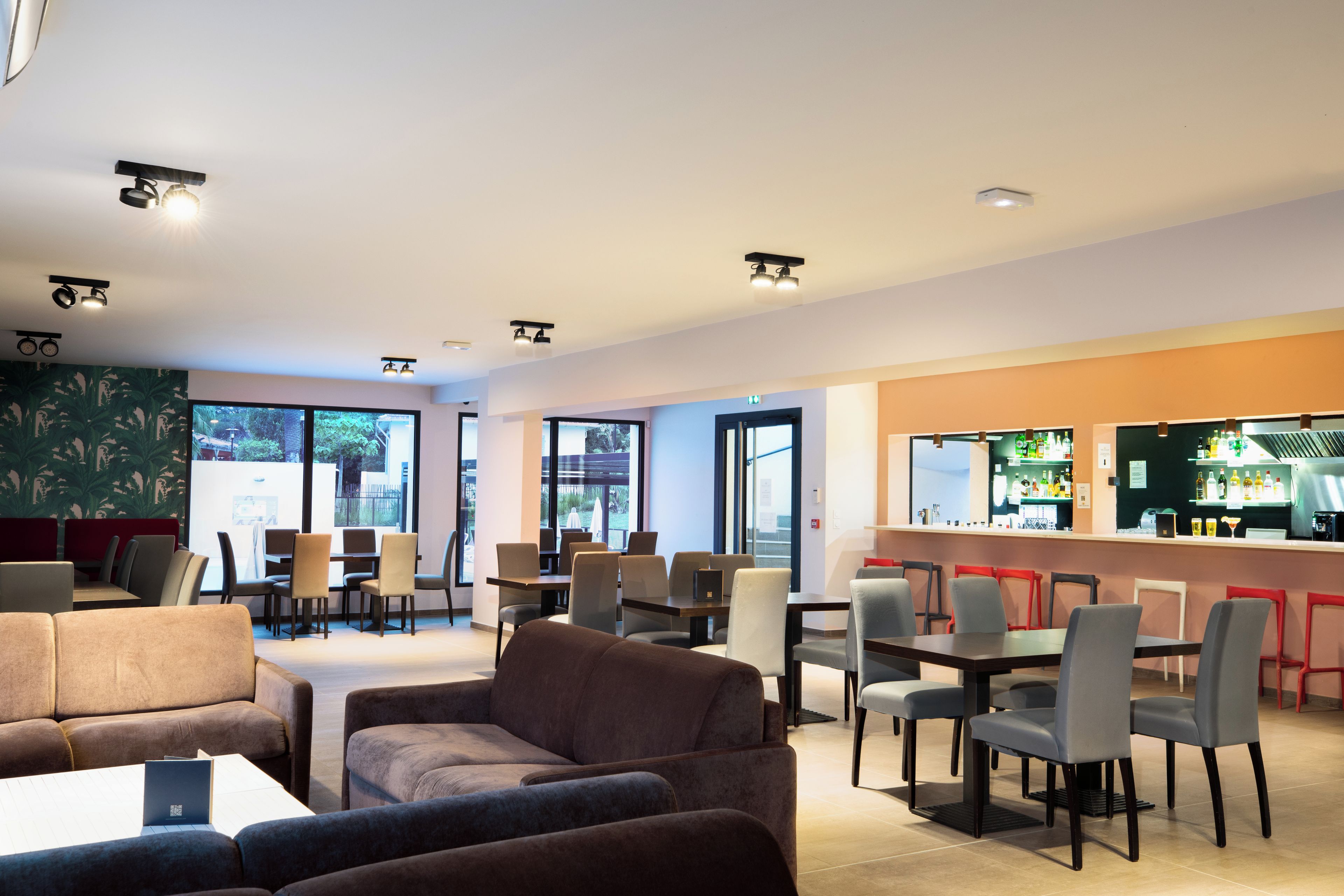 A modern cafe with seating arrangements, a bar area, and large windows providing natural light.