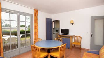 Een compacte kamer met een eettafel en stoelen, een kitchenette met een magnetron, en een televisie.