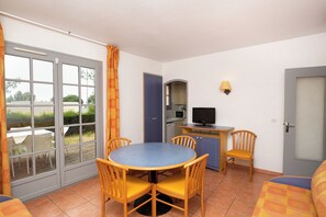 A compact room with a dining table and chairs, a kitchenette with a microwave, and a television. - Sowell Residences Les Chenes Verts (Saint-Raphael)