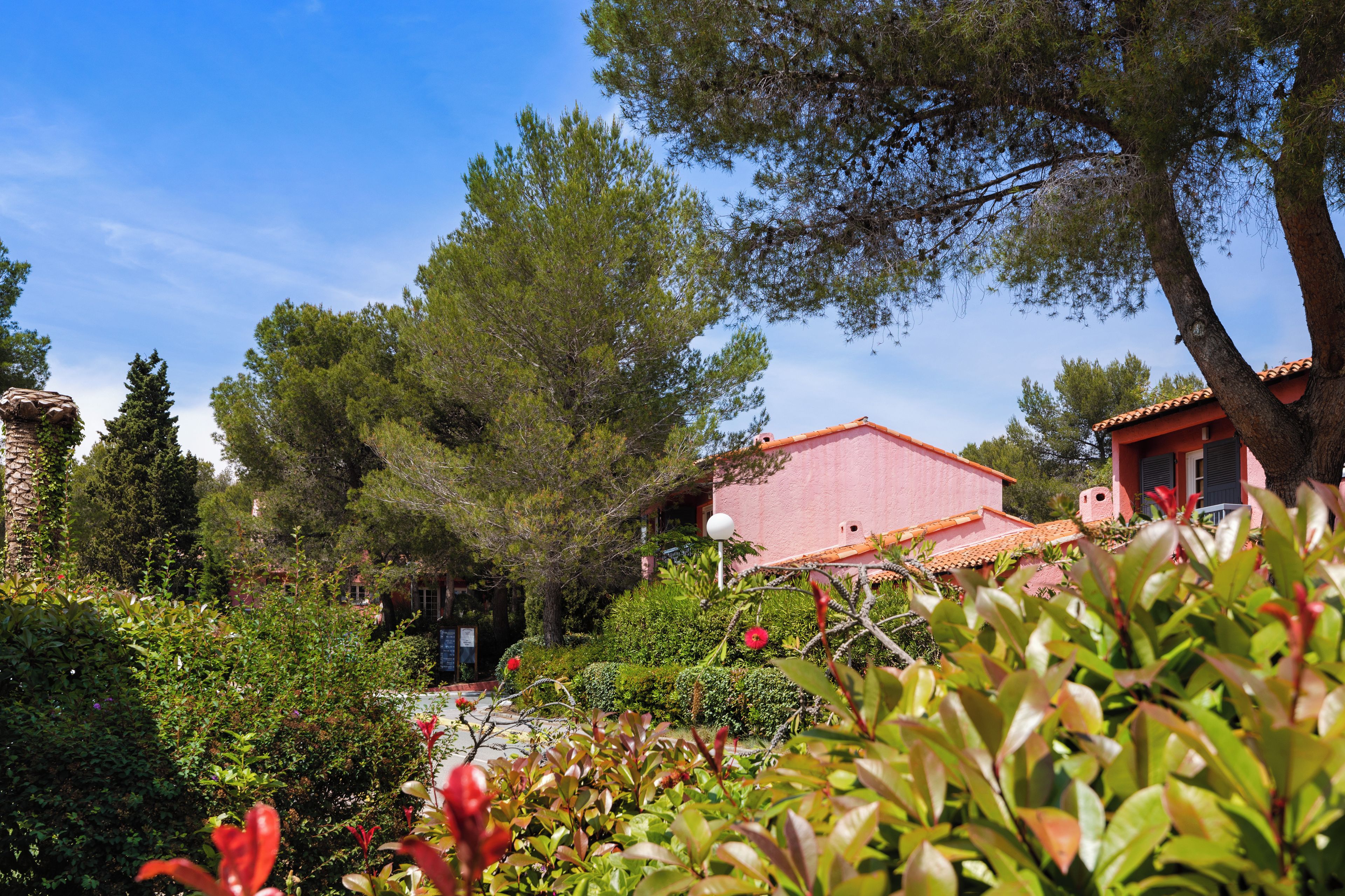 A garden with a red building, surrounded by trees and shrubs.