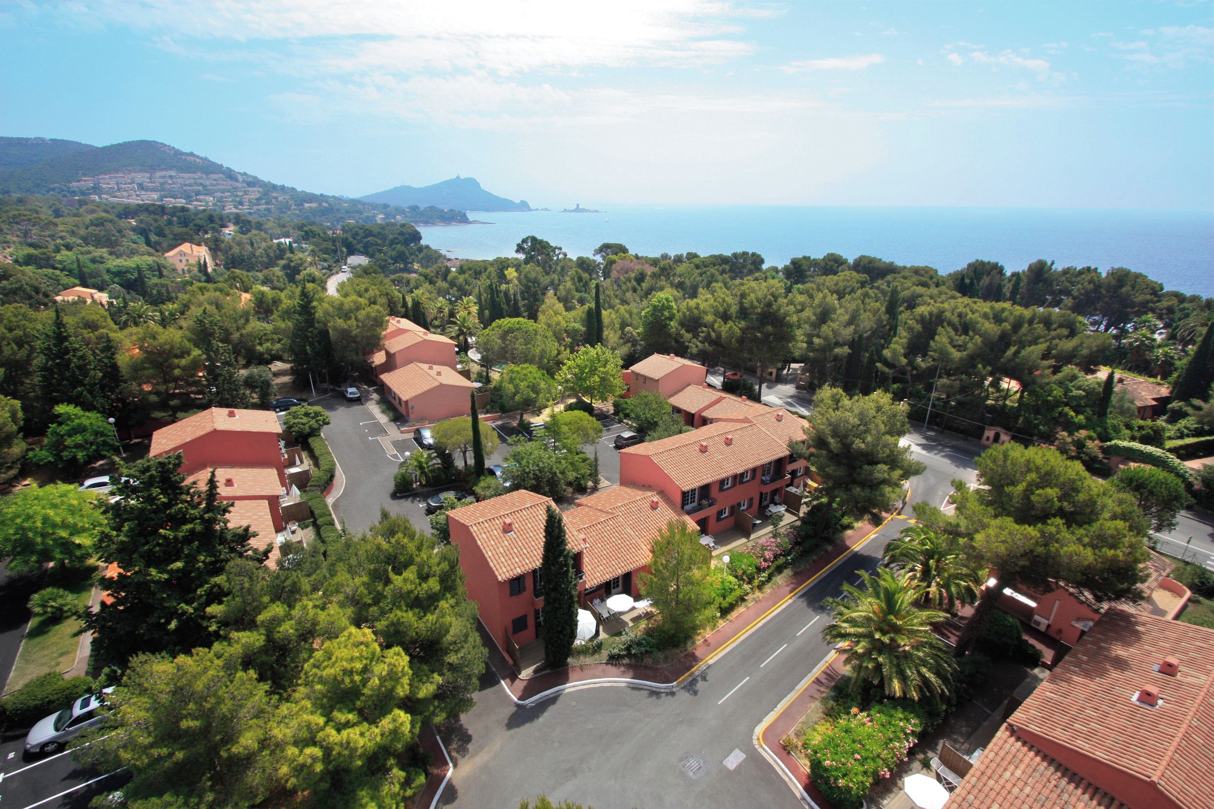 A residential area with red-roofed buildings, green trees, and a view of the sea.