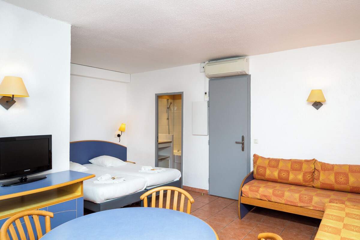 A hotel room with a bed, a desk with a television, a sofa, and two wall-mounted lamps.
