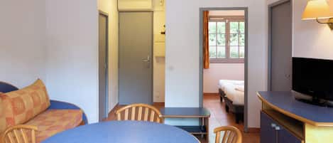A compact hotel room with a dining area, a bed, a television, and a window with curtains.