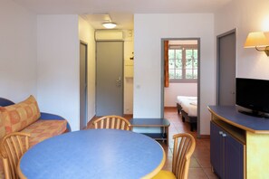 A compact hotel room with a dining area, a bed, a television, and a window with curtains. - Sowell Residences Les Chenes Verts (Saint-Raphael)