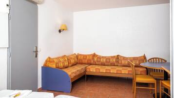 A room with a sofa, a small table, and a chair. There is a door with an air conditioning unit and a wall-mounted lamp.