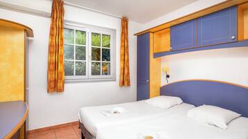 A hotel room with a bed, a desk, a window with curtains, and a blue headboard.