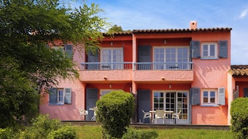 A two-story house with a balcony, a door with shutters, and a small garden area.